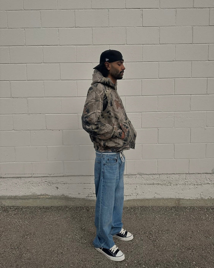 forest camo hoodie worn in profile against a concrete block wall